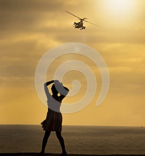 Silhouette of a woman looking out at a helicopter  flying over the ocean