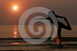 Silhouette of woman making yoga on the beach with sunset background