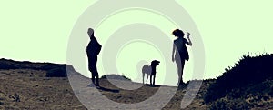 Silhouette of woman, man, and dog taking a walk on the hill.