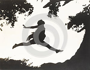 Silhouette of a woman in mid-air jumping between two trees