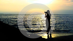 Silhouette of a woman photographer on a beach at sunrise.