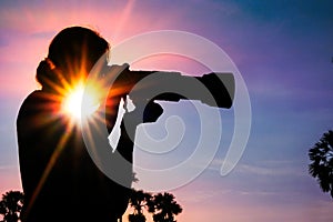 Silhouette of woman photographer in a palm tree garden at sunrise