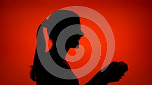 Silhouette of woman play video game online. Female in profile with game console on red background