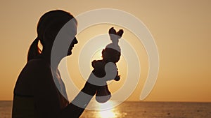 Silhouette A woman is playing with a toy bunny at dawn. Remember childhood