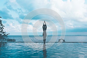 Silhouette woman practice yoga lotus pose to meditation summer vacation on the pool above the beach