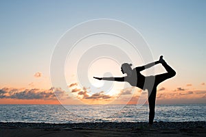 Silhouette of woman practicing authentic yoga on the beach at sunset