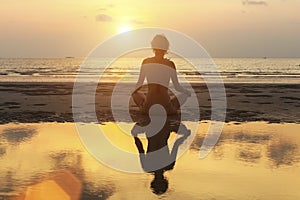 Silhouette woman practicing yoga on the beach at amazing sunset.