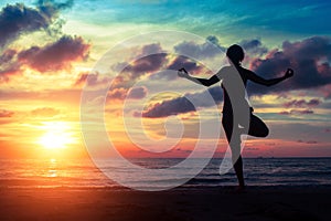 Silhouette woman practicing yoga on the beach at sunset.