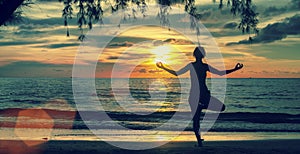 Silhouette woman practicing yoga on beach at surrealistic sunset.