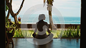 Silhouette of woman is practicing yoga meditation in lotus position on the ocean beach, beautiful view, sounds of nature 
