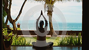 Silhouette of woman is practicing yoga meditation in lotus position, stretches hands up on the beach, beautiful view, nature sound