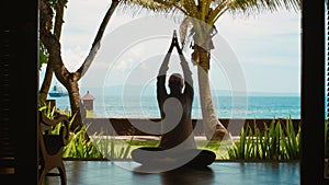 Silhouette of woman is practicing yoga meditation in lotus position, stretches hands up on the beach, beautiful view, nature sound