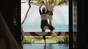 Silhouette of woman is practicing yoga meditation in tree position, stretches hands up on the beach, beautiful view, nature sound