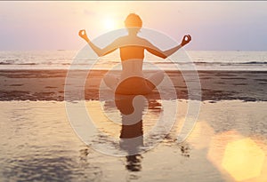 Silhouette woman practicing yoga on Ocean beach at surrealistic sunset.