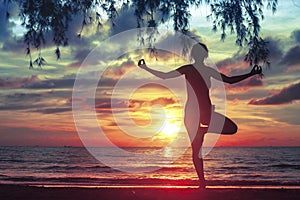 Silhouette woman practicing yoga on the sea beach at blood-surrealistic sunset.