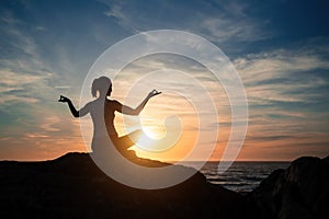 Silhouette woman practicing yoga on the sea beach at  sunset