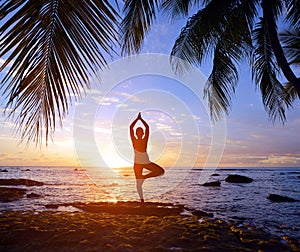 Silhouette of a woman practicing yoga by the tropical sea at sunset.