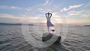 Silhouette of woman is practicing yoga. Woman is meditating on stone at sea shore. Calm and self control. Slow motion