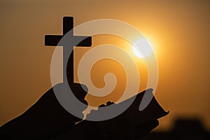 Silhouette of woman praying while holding Bible and cross, Pray in the Morning , Woman praying with hands together on the Sunrise