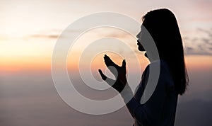 Silhouette of Woman praying for thank god praying with her hands together to think of a loving God, we praise God with light