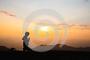 Silhouette of Woman praying for thank god praying with her hands together to think of a loving God, we praise God with light