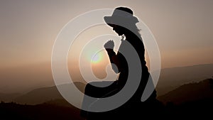Silhouette of Woman praying for thank god praying with her hands together to think of a loving God, we praise God with light flare