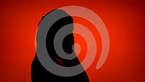 Silhouette of woman putting on headphones on red background. Female face in profile listen to music