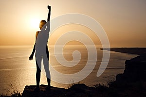 Silhouette of woman with raised hands on the beach at sunset