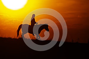 Silhouette of a woman riding a horse with the setting sun