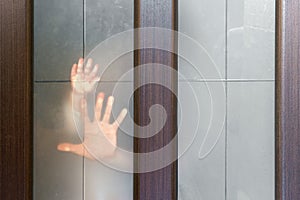 Silhouette of woman`s and child`s hand, palm behind frosted, opaque glass of wooden door. concept of single-parent family. Raisi