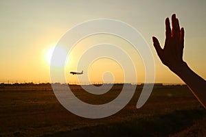 Silhouette of woman`s hand waving to the airplane against sunset sky