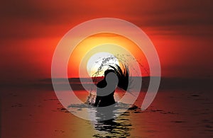 Silhouette of Woman in the sea at sunset flipping her hair out of the water