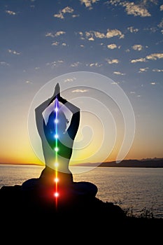 Silhouette of woman sits in a lotus pose on beach sunset view, glowing seven all chakra. Kundalini energy. girl practicing yoga