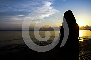 Silhouette woman sitting and looking sunrise at sea