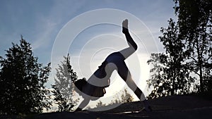 Silhouette of woman with sporty flexible body performing Three-Legged Downward-Facing Dog pose