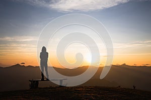 Silhouette of a woman standing alone on the top of a mountain and watching the sunrise