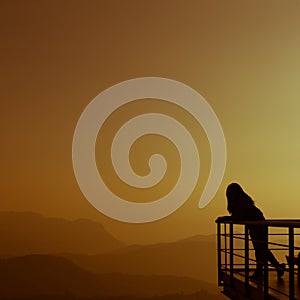 Silhouette of the woman standing lonely at the balcony in mountain background during sunrise time.