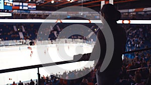 Silhouette of woman standing and watching players during practice. Moment before start of ice hockey match. Concept of