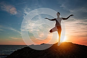 Silhouette of woman standing at yoga pose on the sea beach.