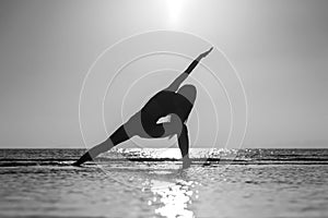 Silhouette of woman standing at yoga pose on the tropical beach during sunset. Girl practicing yoga near sea water. Black and