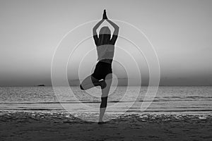 Silhouette of woman standing at yoga pose on the tropical beach during sunset. Girl practicing yoga near sea water. Black and