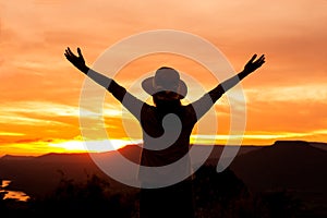 Silhouette woman stands on mountain top at sunset time