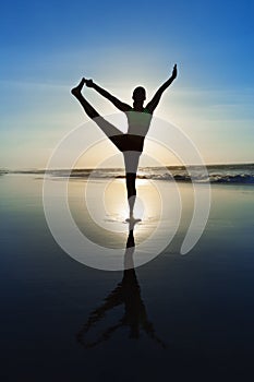 Silhouette of woman stretching at yoga pose on sunset beach