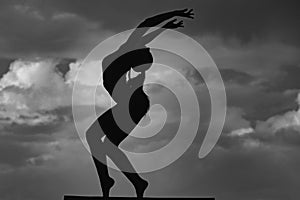 Silhouette of woman stretching. Young girl practicing yoga, doing fit exercise, working out. Dance studio. Cloudy sky