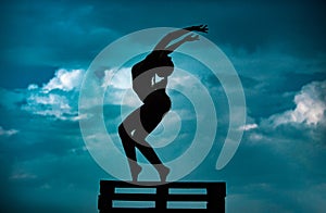 Silhouette of woman stretching. Young girl practicing yoga, doing fit exercise, working out. Dance studio. Cloudy sky