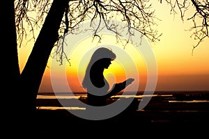 Silhouette of a woman studing the Bible in nature at sunset, concept religion and spirituality photo