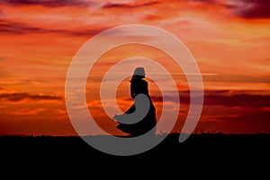 Silhouette of a woman in sunset with dress and hair blow by the wind