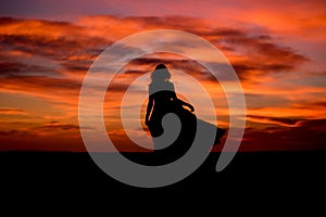 Silhouette of a woman in sunset with dress and hair blow by the wind