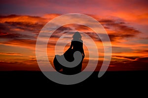 Silhouette of a woman in sunset with dress and hair blow by the wind