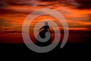 Silhouette of a woman in sunset with dress and hair blow by the wind